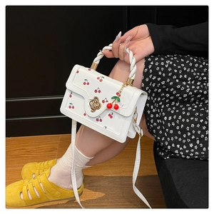 Détail du sac bandoulière blanc à imprimé cerise avec fermoir doré en forme de fleur
