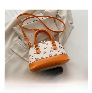 Close-up of shell-shaped mini handbag with cherry prints beside a phone for scale