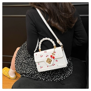 Détail du sac à motif cerises avec fermoir fleur en métal et poignée supérieure tissée