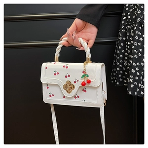 Detail of white mini bag featuring red cherry prints and golden flower metal buckle