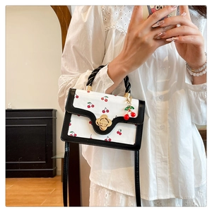Détail du sac bandoulière à motif cerises, poignée tressée noire et fermoir camélia doré