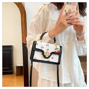 Close-up of white cherry print handbag with golden camellia clasp and cherry charm