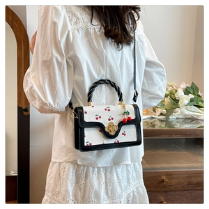 Détail du sac à main cerise avec fermoir floral doré et poignée tressée sur modèle