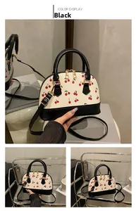 Detail view of cherry print shell bag with black leather handles and golden zippers