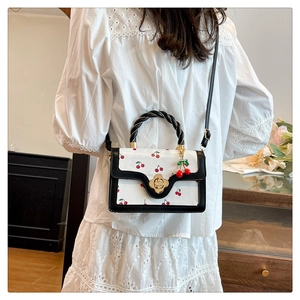 Detail showing white cherry print crossbody bag with gold flower buckle and cherry charm