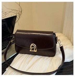 Détail d'un sac bandoulière en cuir brillant marron foncé avec boucle métallique dorée