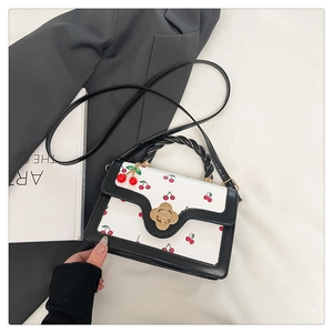Close-up of red cherry print on contrast shoulder bag with golden floral twist lock