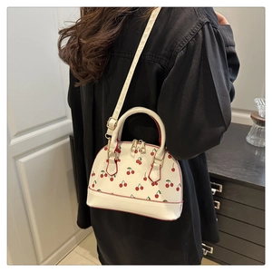 Close-up of a white shell handbag with cherry print held by a model in black clothing