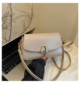 Détail d'un sac bandoulière en cuir PU beige avec boucle dorée sur un bureau moderne