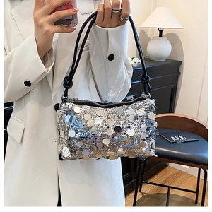 Close-up of shiny silver sequin shoulder bag held by a model in a white blazer outfit