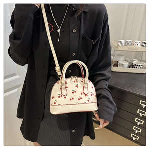 Detailed view of white shell crossbody bag with red cherry print and dual top handles