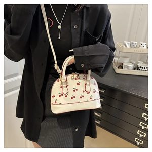 Detail of white shell bag featuring red cherry print and adjustable long shoulder strap