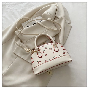 Close-up of cherry print bucket bag with red trim and golden hardware on beige blazer