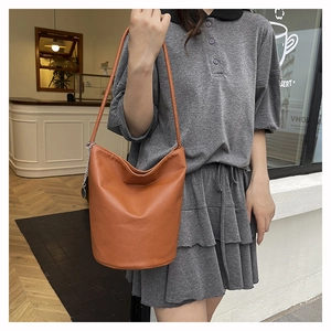 Brown leather bucket bag detail with textured finish and decorative metal chain hanging