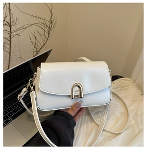 Gros plan d'un sac bandoulière blanc avec fermoir doré dans un décor de style de vie