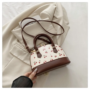 Detail of cherry print shell bag with brown leather handles and gold metal hardware