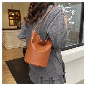 Detail of caramel leather bucket bag featuring lychee grain texture and silver chain charm
