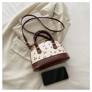 Top view of cherry print bucket bag on beige blazer with phone for size reference
