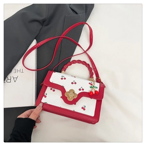 Detail of cherry print handbag with gold flower clasp and woven handle on a suit background