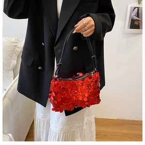 Close-up of red sequin shoulder bag with black leather strap held by a model