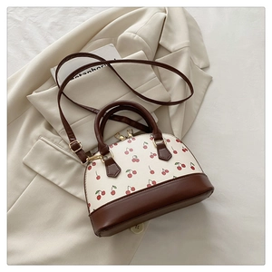 Detail of a cherry print shell bucket bag featuring brown leather trim and golden hardware