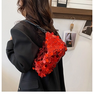 Detail of red sequin shoulder bag with black strap worn by model against a white wall
