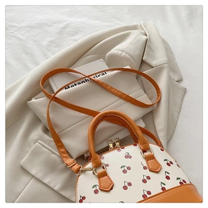 Detail of cherry print bucket bag with orange faux leather straps and gold metal hardware