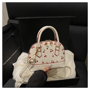 Detail of cream cherry shell bag with golden hardware and adjustable shoulder strap