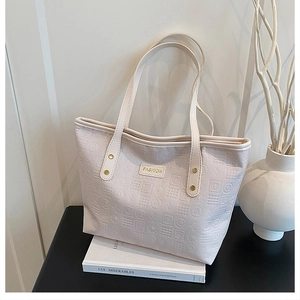 Detail view of cream tote bag with embossed textures and a golden Fashion metal plaque