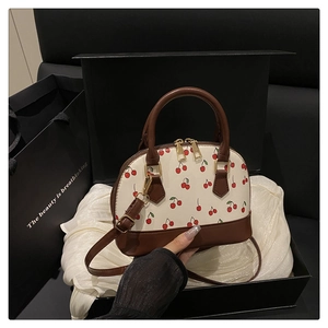 Detail of cherry print shell bag with brown leather handles on elegant gift box