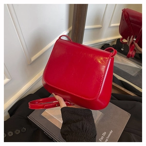 Close-up of bright red glossy patent leather saddle bag with gold metal buckle