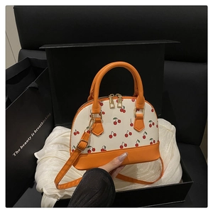 Detail of cherry print shell bag with orange leather trim inside a black gift box