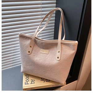 Detail of beige tote bag featuring embossed geometric patterns and gold metal logo