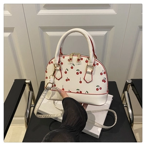 Detail of white cherry print bucket bag with gold hardware and leather top handles