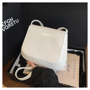 Glossy white faux leather saddle bag displayed in a premium black gift box setup