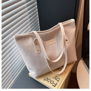 Gros plan du sac fourre-tout crème avec motifs géométriques gaufrés et plaque dorée élégante