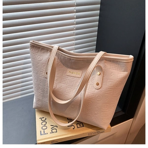Detailed macro view of embossed leather texture and gold logo plaque on a chic beige tote bag