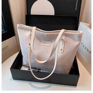 Detail of white leather tote bag featuring embossed patterns and gold metal brand name tag