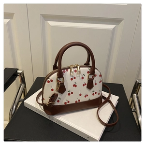 Detail of cherry print bucket bag with gold zippers and brown leather trim on books