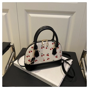 Detail of cherry print handbag with double zippers and gold hardware on white surface