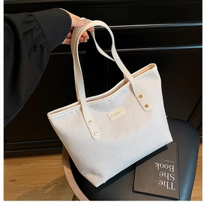 Gros plan d'un cabas en cuir crème avec motifs embossés et détails de rivets dorés