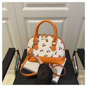 Detail of cherry print shell bag with orange handles and gold zipper closure