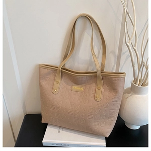 Detail of beige embossed tote bag with metal Fashion logo plaque on a book