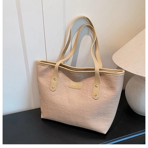 Close-up of beige faux leather tote bag with geometric letter embossing and metal brand tag