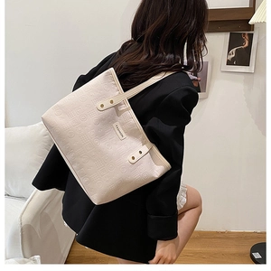 Detailed view of beige embossed tote bag with Fashion tag worn by a model in a black suit