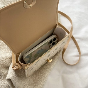 Straw saddle bag with floral lace patterns and gold twist lock shown with a phone inside
