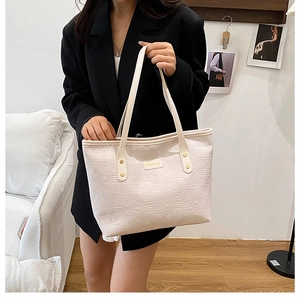 Gros plan sur un sac cabas blanc crème avec motifs gaufrés et rivets dorés