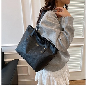 Detail of black embossed leather tote bag showing geometric texture and gold metal studs
