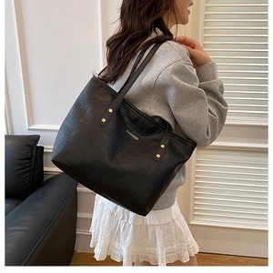 Detail of black embossed leather tote bag featuring gold fashion plaque and metal studs
