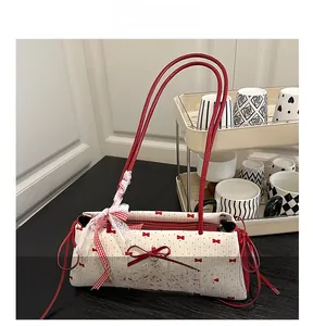 Détail du sac bandoulière en toile blanche avec imprimé nœud rouge et pendentif cœur